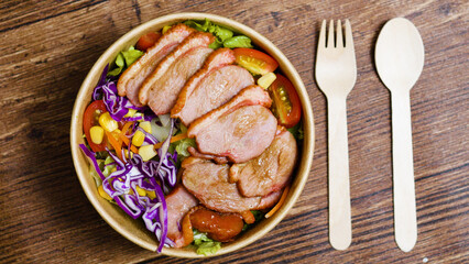Gourmet salad featuring smoked duck breast, crisp lettuce, ripe tomatoes, sweet corn, vibrant red cabbage in rustic takeaway bowl on wooden surface, highlighting fresh, nutritious dining