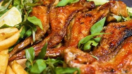 Sizzling roasted chicken wings seasoned with herbs and spices, served alongside crispy golden french fries and lime wedges, creating a mouthwatering culinary experience