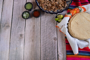 Top view of a table with tortillas, meat for pork carnitas, and various salsas, with space for text