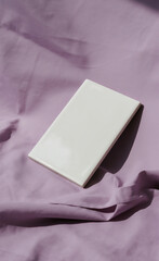 Modern Surface Design: A Clean Rectangular White Ceramic Tile Mockup, Artfully Placed on a Wrinkled Lavender Fabric Background with Distinct Sunlight and Shadows, Perfect for Interior Decor 