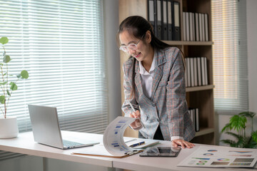 woman is sitting at a desk with a laptop and a stack of papers