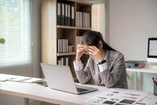 woman is sitting at a desk with a laptop and a stack of papers - Powered by Adobe