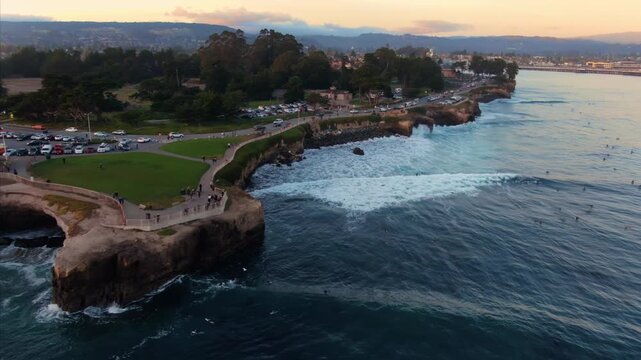 An aerial view of surfers enjoying the waves at Steamer Lane in Santa Cruz, California, USA. People are watching from the cliffside near the Mark Abbott Memorial Lighthouse.