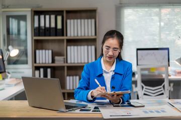 Fototapeta premium woman in a blue jacket is sitting at a desk with a laptop and a notebook