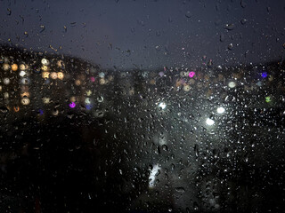 The window is wet from rain. Theme Background.Night city behind wet glass. Urban