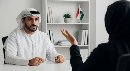 A man in traditional Middle Eastern attire attentively listens to a woman in a hijab during a serious business meeting.