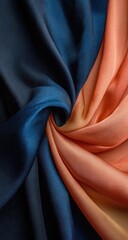 Fototapeta premium Swirling draped fabric, deep blue contrasting with shades of orange and peach. The material is lustrous, possibly silk or satin, folded into a vortex-like shape