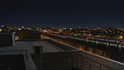 The cityscape glitters at night, as a train makes its way across the illuminated tracks. A breathtaking nighttime view of the urban landscape, featuring buildings and architecture. 