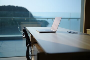 Modern office desk with laptop and phone overlooking scenic ocean view chair