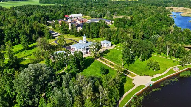 Aerial parallax movement reveals Astravas Manor, an Italian villa-style palace, nestled in lush parkland beside a scenic lake in Biržai, Lithuania.