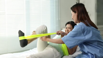 Professional physiotherapist helping senior woman with physical therapy exercises using elastic band, promoting mobility and recovery in a rehabilitation center.
