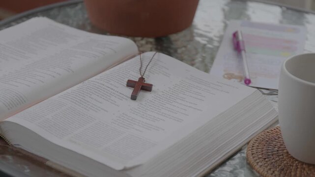 Open Bible with a wooden cross necklace laid on its pages, accompanied by study notes and a pen