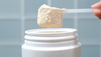 Hand takes protein powder in scoop from plastic jar top view on blue tile background close-up. - Powered by Adobe