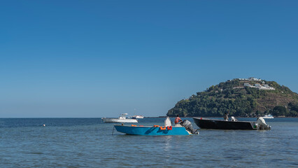 Obraz premium Motor boats are anchored in the blue ocean. White buildings on a green hill. Clear azure sky. Copy space. Madagascar. Nosy Be 