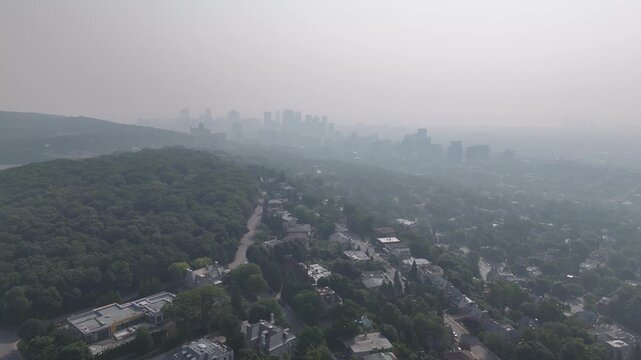 Hazy aerial view of Westmount and downtown Montreal skyline hidden behind smog and trees. c.