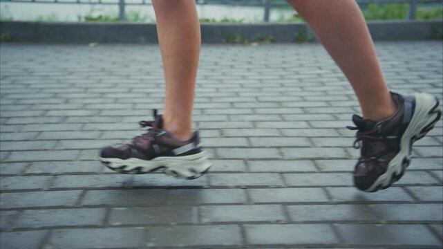 Dynamic close-up of a runner's legs in motion showcasing athletic shoes on a pavement path, highlighting speed and energy during a workout session. - Powered by Adobe