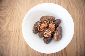 Whole and half nutmeg in white bowl isolated on wooden background