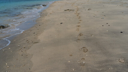 A chain of human bare footprints stretched along the ocean shore. Prints on wet sand. The waves of the turquoise sea are foaming. Madagascar.