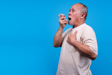 Elderly Asian Man Using Inhaler To Relieve Breathing Difficulties Clutching His Chest In Discomfort
