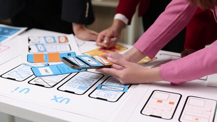 User experience and user interface designers collaborate on a project, arranging paper prototypes on a table to enhance mobile app usability. - Powered by Adobe