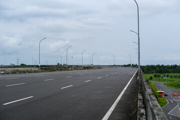 Fototapeta premium Empty road stretches over a bridge under cloudy skies, surrounded by green fields and minimal traffic, offering a quiet scene of infrastructure and open space. Road in pandemic time.