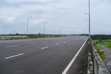Empty road stretches over a bridge under cloudy skies, surrounded by green fields and minimal traffic, offering a quiet scene of infrastructure and open space. Road in pandemic time.