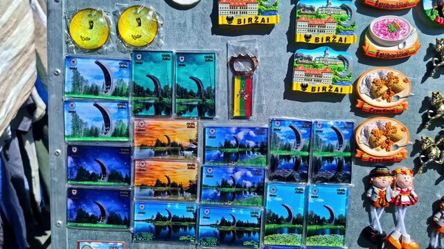 A vibrant collection of Birzai, Lithuania souvenir magnets featuring landmarks, foods, and traditional costumes arranged on a metal display at a market.