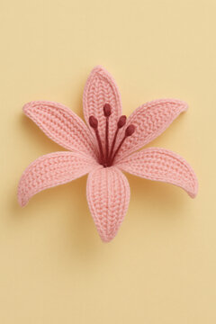 A delicate, handmade knitted flower with light pink petals and dark red stamens, set against a soft yellow backdrop.