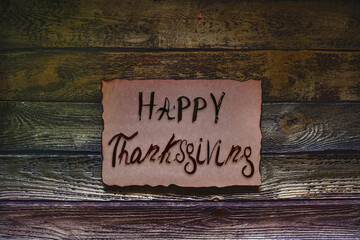 Happy thanksgiving. Hand drawn calligraphy, paint brush lettering.Text on craft beige weathered paper with burn marks, dark golden brown wooden  wall. Design holiday greeting card,  invitation.