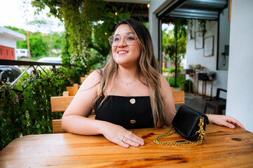 Young Woman Smiling at Outdoor Café Table with Natural Green Background