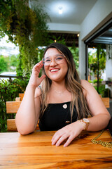Young Woman Smiling at Outdoor Café Table with Natural Green Background
