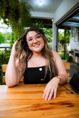Young Woman Smiling at Outdoor Café Table with Natural Green Background
