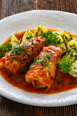Stuffed cabbages with tomato sauce and boiled potatoes on wooden table - polish cuisine golabki