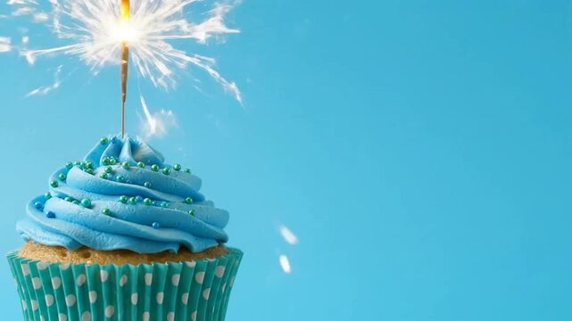 A bluefrosted cupcake topped with a sparkler set against a plain blue background