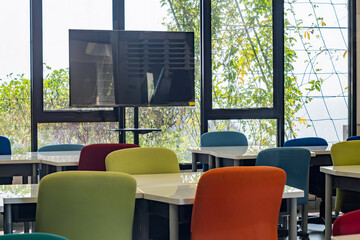 Colorful classroom interior with modern furniture, a TV, and large windows overlooking a leafy landscape.