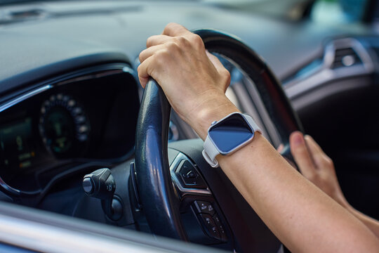 Close-up of hands holding steering wheel inside modern car with dashboard in background. Woman driving car