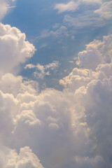 A stunning aerial view above the clouds, with soft, billowing cumulus formations revealing glimpses of the blue sky and earth below, bathed in gentle sunlight for a dreamy, serene effect.