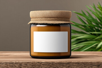 Amber glass jar with blank white label and burlap cover on wooden surface with plant in background