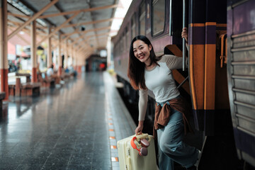 Happy tourist boarding a train at the railway station, holding her trolley and eagerly preparing...
