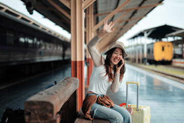 Happy tourist waving and chatting on the phone while waiting for the train's arrival at the...