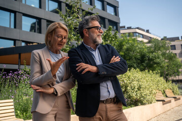 Fototapeta premium Mature businessman and businesswoman arguing outdoors in urban business district, misunderstanding and conflict during stressful professional conversation 