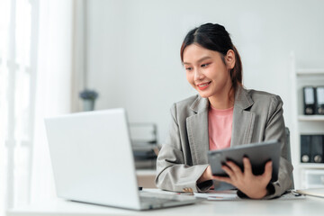 Young professional woman sitting at a desk, comparing information on a laptop and tablet while...