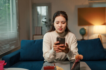 Young Asian woman relaxing on the sofa in her living room at night, wearing a beauty mask while...