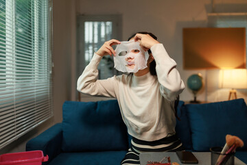 Young woman wearing a white sweater and a striped skirt is sitting on a blue sofa in her living...