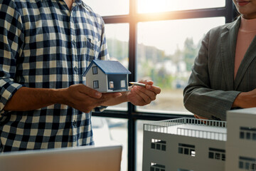 Architect holding a small house model, explaining project details with a pen to the manager....