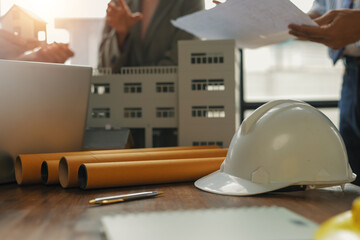 Architects and engineers are discussing building project with blueprints and scale model on the...
