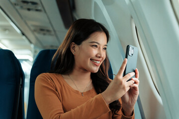 Happy passenger smiling while capturing moments with her smartphone during a flight, relishing the journey and enjoying breathtaking views from the airplane window