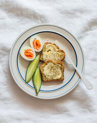 Delicious breakfast - toasts with butter, boiled egg, fresh cucumber on a plate on a light background, top view