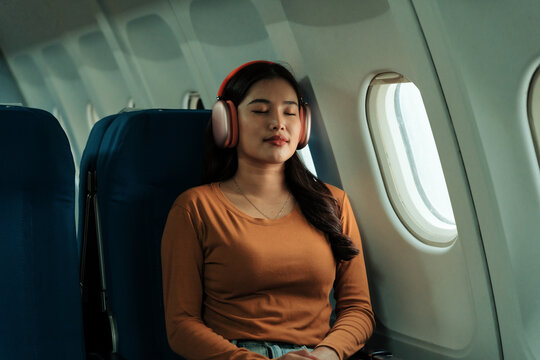 Relaxed tourist enjoying music during a flight, wearing comfortable clothes and noise canceling headphones, sitting near the window of an airplane