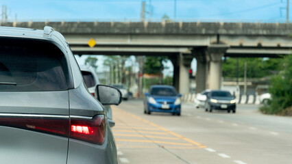 Rear side of silver car with turn on brake light. Stop by traffic control in the junction. Background with other cars driving from the opposite lane. With concrete bridge under blue sky.